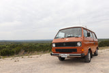 This orange VW Vanagon high-top camper is perfect for an RV rental adventure, parked on a scenic Texas overlook.