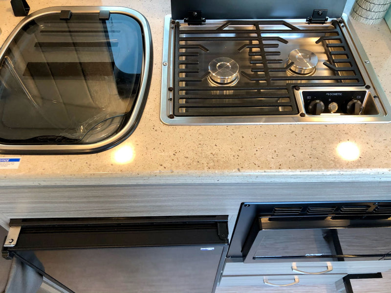 This rv rental features a compact kitchen: covered sink, 2-burner Dometic cooktop, and under-counter fridge and microwave. — photo 7