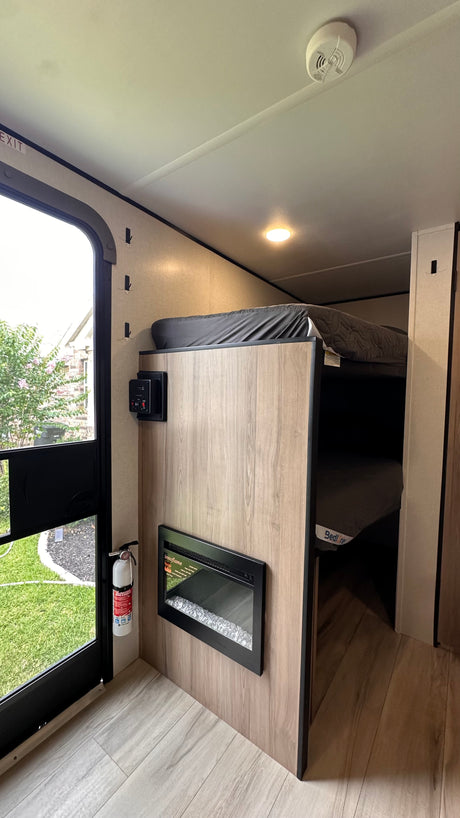 RV rental interior features bunk beds, a wall-mounted electric fireplace, and controls. Safety includes an extinguisher by the exit.