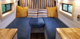 Cozy RV rental interior featuring blue U-shaped seating with colorful pillows, framed windows, and wooden countertops.
