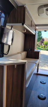 Modern RV rental interior with sleek dark wood cabinetry, light upholstered seating, a TV, and floor mounts, inviting the outdoors in.