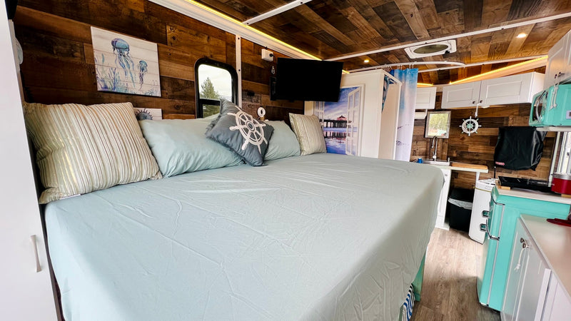 Spacious RV rental interior featuring a large bed, nautical decor, compact kitchen with retro fridge, and shower. — photo 7