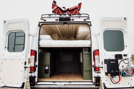 This RV rental reveals a camper van's open rear, showcasing a cozy bed, storage, and outdoor shower setup, perfect for adventure.