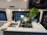 Cozy RV rental kitchen with a sink, stovetop, moka pot, and microwave, adorned with a plant. Perfect for road trip meals!