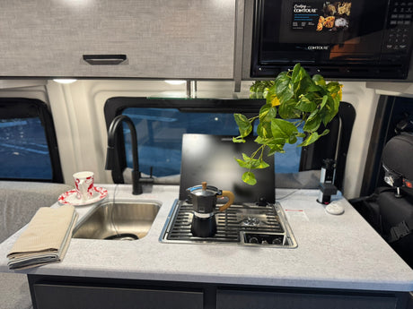 Cozy RV rental kitchen with a sink, stovetop, moka pot, and microwave, adorned with a plant. Perfect for road trip meals!