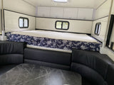 Spacious RV rental interior. Features a large bed with floral bedding, U-shaped black seating, and a dining table.