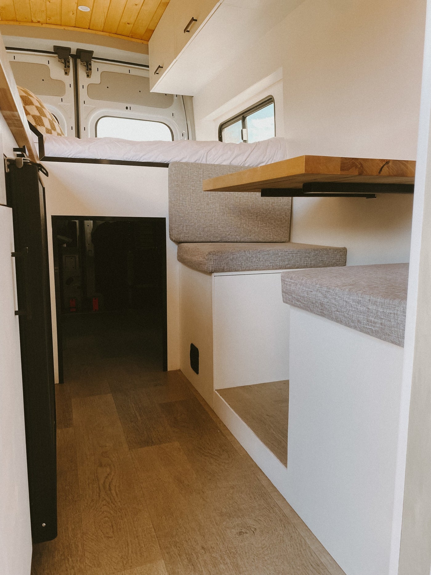Explore the interior of this modern RV rental: a compact camper van with an elevated bed, comfy dinette, and sleek wood design. — photo 5