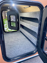 Explore this RV rental's cozy, carpeted interior, featuring integrated shelving for storage and ample space for sleeping.