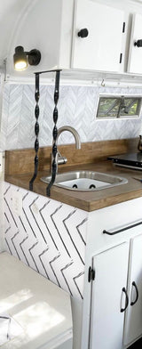 Modern RV rental kitchenette featuring a sleek sink, wood counters, and stylish chevron patterns. Compact & well-equipped.