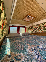 Cozy tropical RV rental interior with a comfortable bed, bamboo ceiling, and floral decor for your adventure.