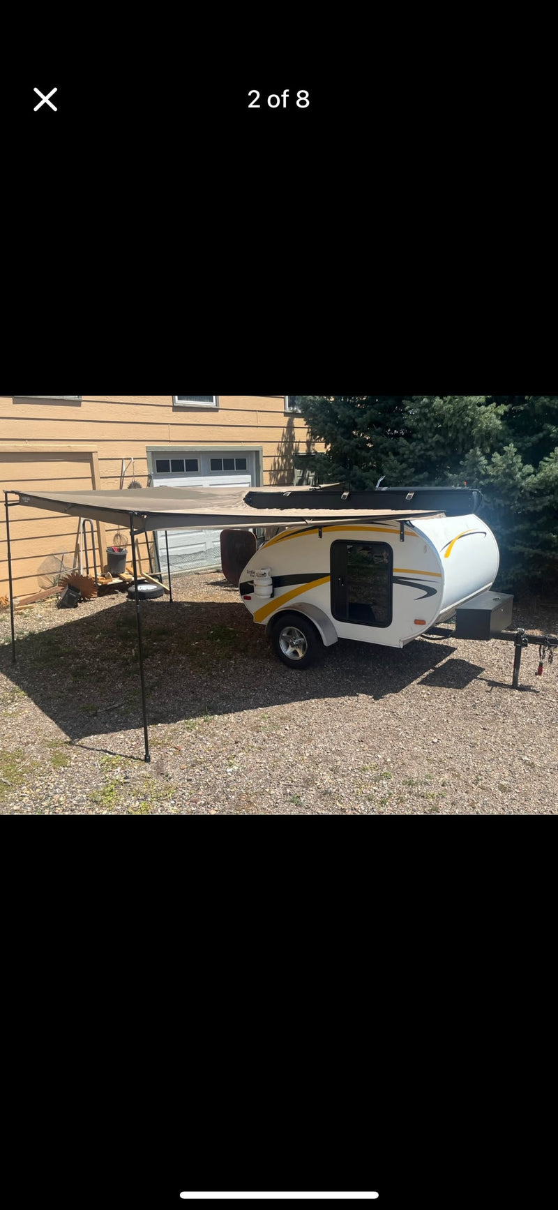 Compact teardrop camper with an awning, ideal for an rv rental adventure. Parked on gravel next to a house. — photo 6
