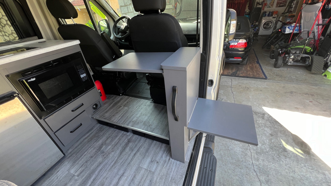 Custom rv rental van interior: kitchen with microwave, sink, and two retractable tables for versatile use.