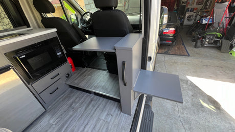 Custom rv rental van interior: kitchen with microwave, sink, and two retractable tables for versatile use.
