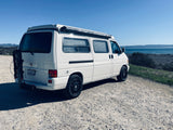 White VW camper van, ideal RV rental for coastal road trips. Parked on a bluff overlooking the ocean.