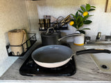 Compact RV rental kitchen with a hot plate, frying pan, saucepan, sink, and wall-mounted storage for spices and towels.