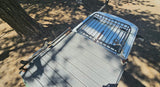 Overhead of an RV rental: custom roof deck, front cargo rack. Parked under dappled tree shade. Ideal for outdoor adventures.