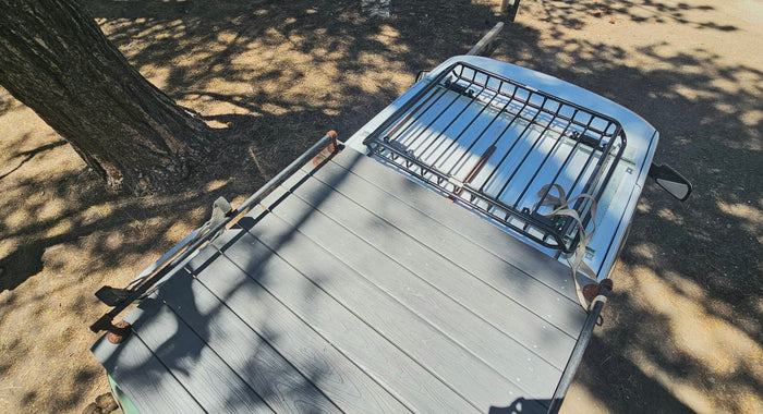Overhead of an RV rental: custom roof deck, front cargo rack. Parked under dappled tree shade. Ideal for outdoor adventures.