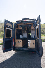 Explore the custom interior of this dark blue camper van, featuring cozy seating and wood paneling, ideal for an RV rental adventure.