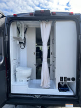 Rear view of an RV rental's interior, showcasing its compact bathroom with toilet, shower, and integrated storage area.