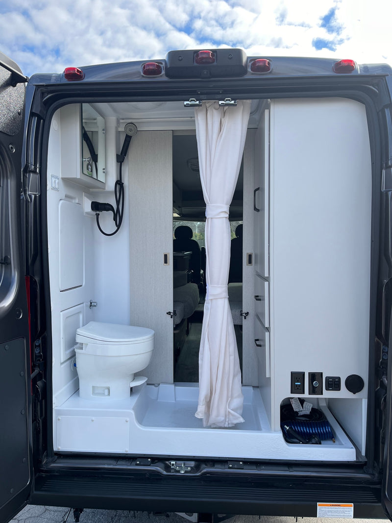 Rear view of an RV rental's interior, showcasing its compact bathroom with toilet, shower, and integrated storage area. — photo 10