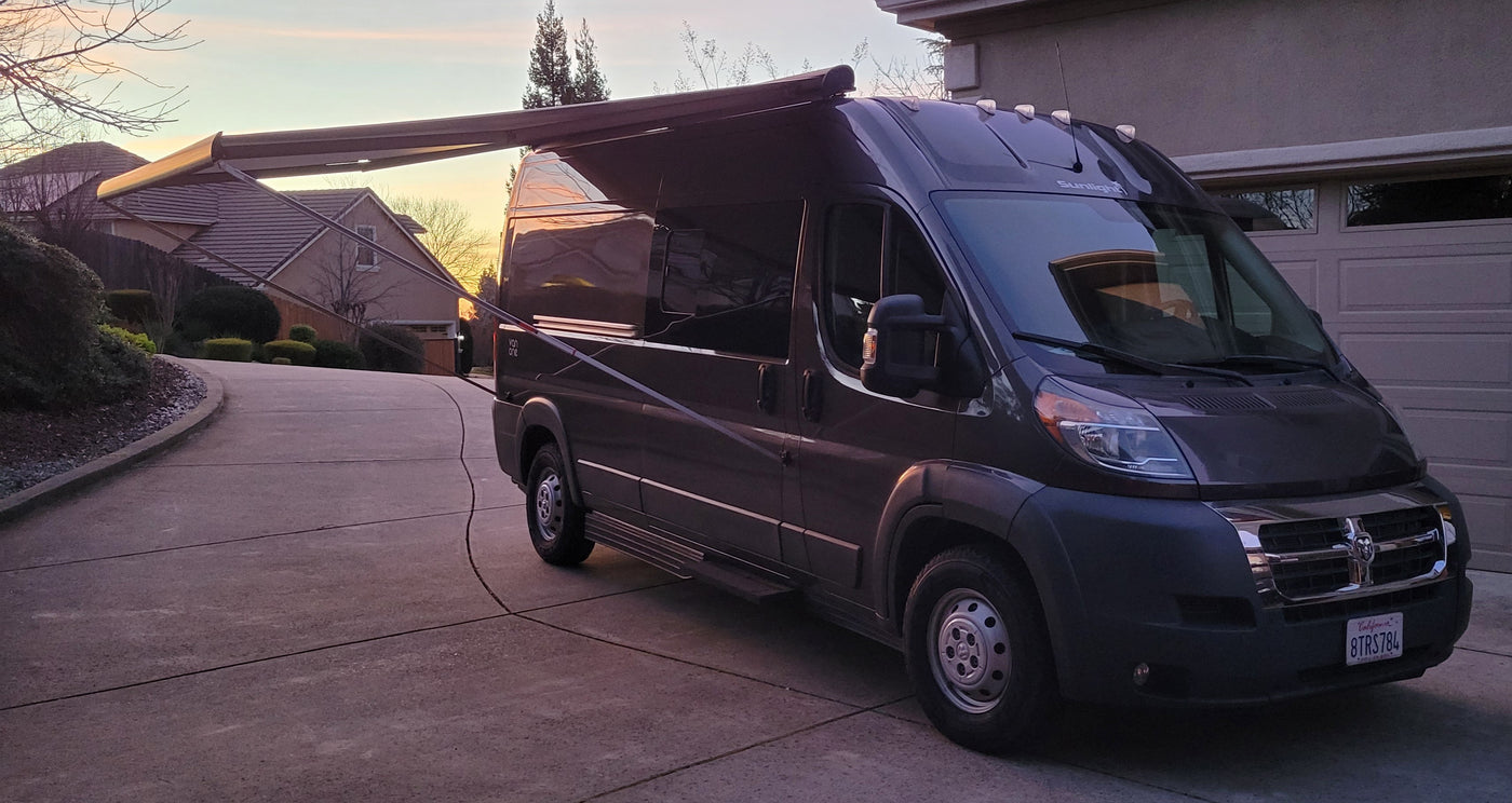A dark grey camper van with extended awning parked on a driveway at sunset. Ideal for your next RV rental adventure. — photo 12