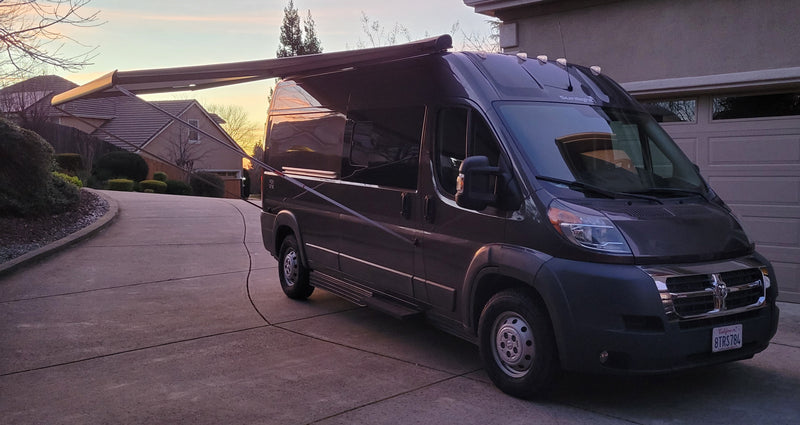 A dark grey camper van with extended awning parked on a driveway at sunset. Ideal for your next RV rental adventure. — photo 12