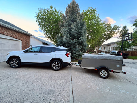 White SUV hitched to a grey Quicksilver compact pop-up camper in driveway, ideal for RV rental trips.