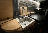 Functional rv rental kitchenette: stainless steel sink, wood counter, portable grill, and textured accent wall.