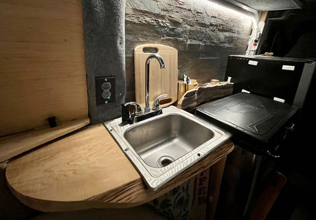 Functional rv rental kitchenette: stainless steel sink, wood counter, portable grill, and textured accent wall.