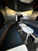 Discover the cozy interior of an RV rental with U-shaped seating, two tables, and sleek aluminum walls.