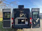 Rear view of an open gray camper van, showcasing interior bed, storage, and utility panel, ideal for an rv rental.