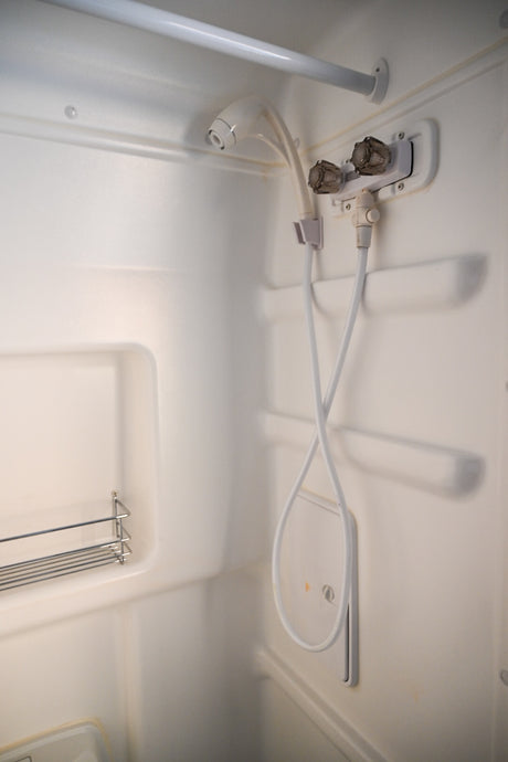 Inside an RV rental shower: white molded stall with handheld shower, water controls, and a wire rack for essentials.