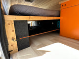 RV rental interior: Cozy bed platform with ample under-bed storage. Features wood paneling, an orange cabinet, and bungee cord.