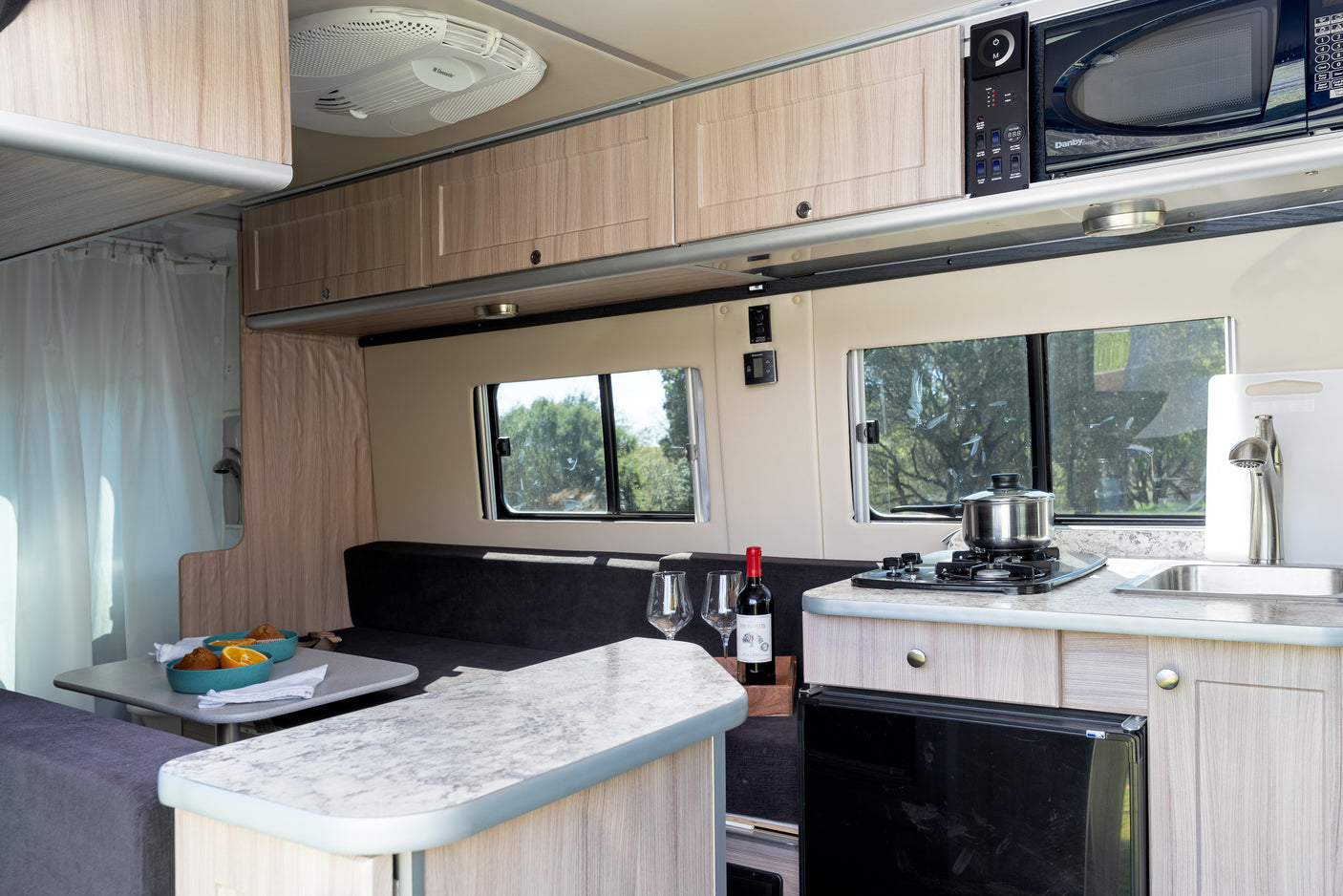 Inside this RV rental: A compact kitchen with stove, sink, and microwave, plus a dining area and comfortable seating.