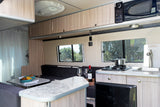 Inside this RV rental: A compact kitchen with stove, sink, and microwave, plus a dining area and comfortable seating.