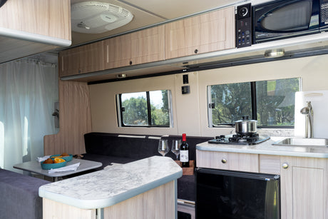 Inside this RV rental: A compact kitchen with stove, sink, and microwave, plus a dining area and comfortable seating.