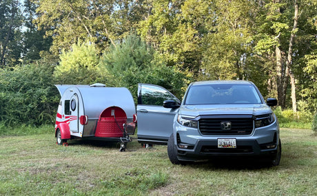 Grey Honda Ridgeline with open door hitched to a silver and red teardrop RV rental, ready for camping.