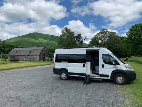 Scenic rv rental stop: white camper van at a farm with a barn, mountains, and hikers.