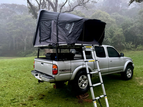 Silver truck with an iKamper rooftop tent deployed, perfect for an overland RV rental trip in a misty forest.