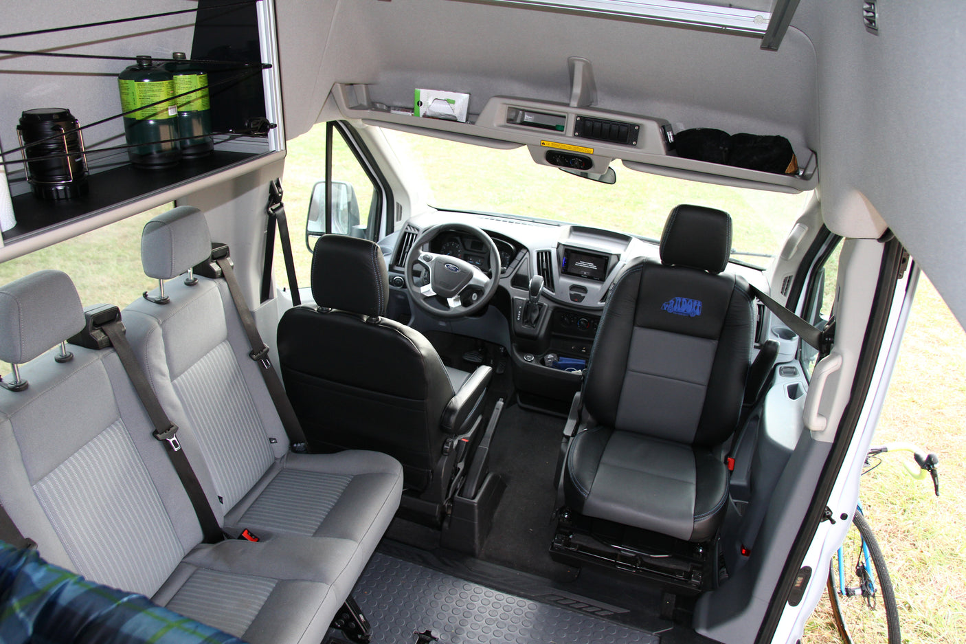 Ford Transit camper van interior: driver's cockpit, passenger seating, and rear storage shelf. Ideal for an RV rental adventure.