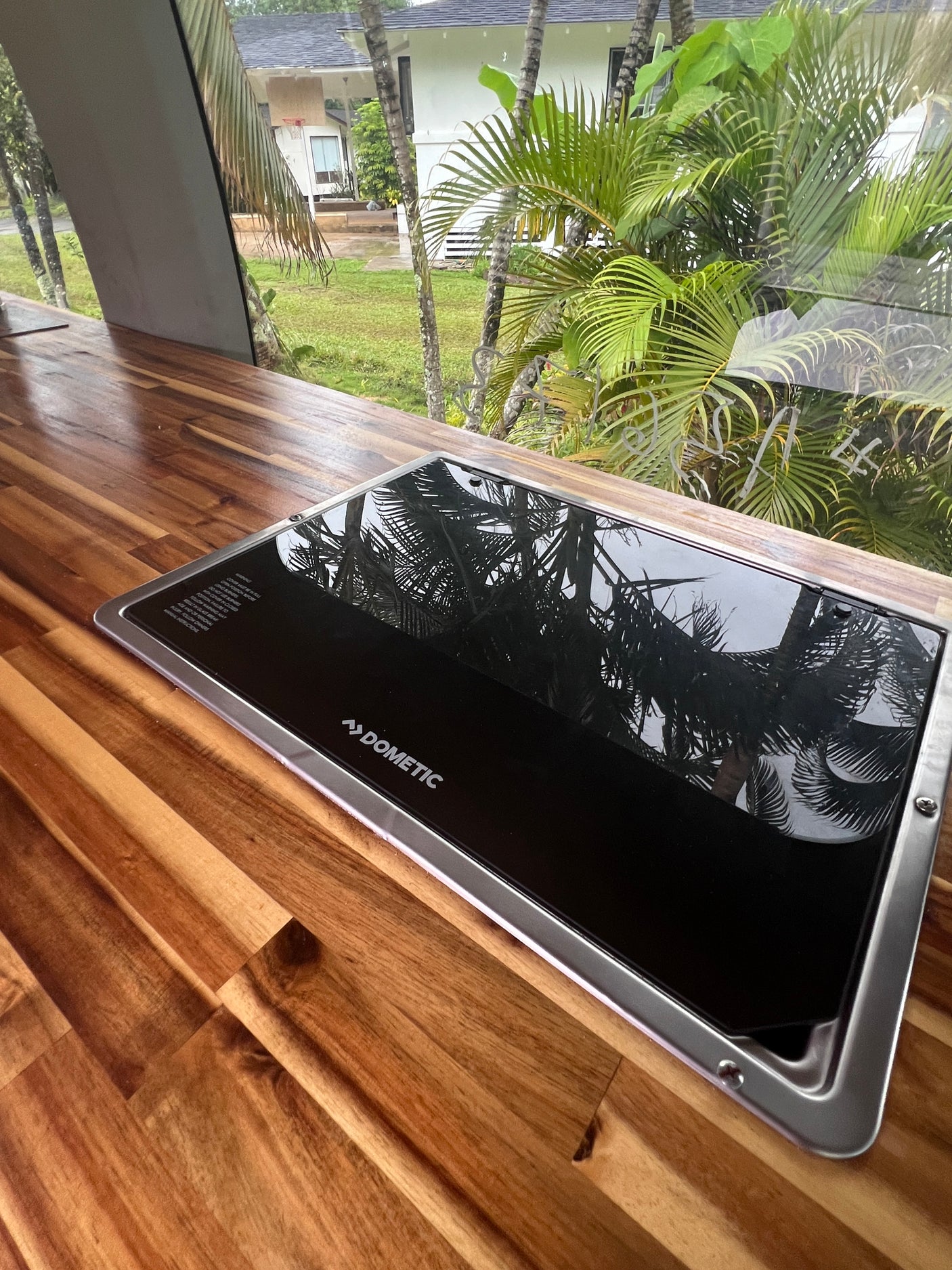 Modern Dometic cooktop on a rich wood counter in this RV rental's kitchen, reflecting the tropical outdoor view.