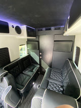 Inside a stylish RV rental: black quilted seating, multiple screens, microwave, and a unique starry ceiling design.