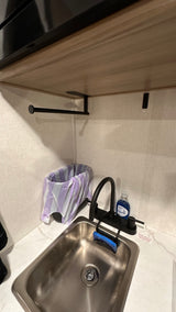 Compact RV rental kitchen area featuring a stainless steel sink, black faucet, dish soap, sponge, and trash can.