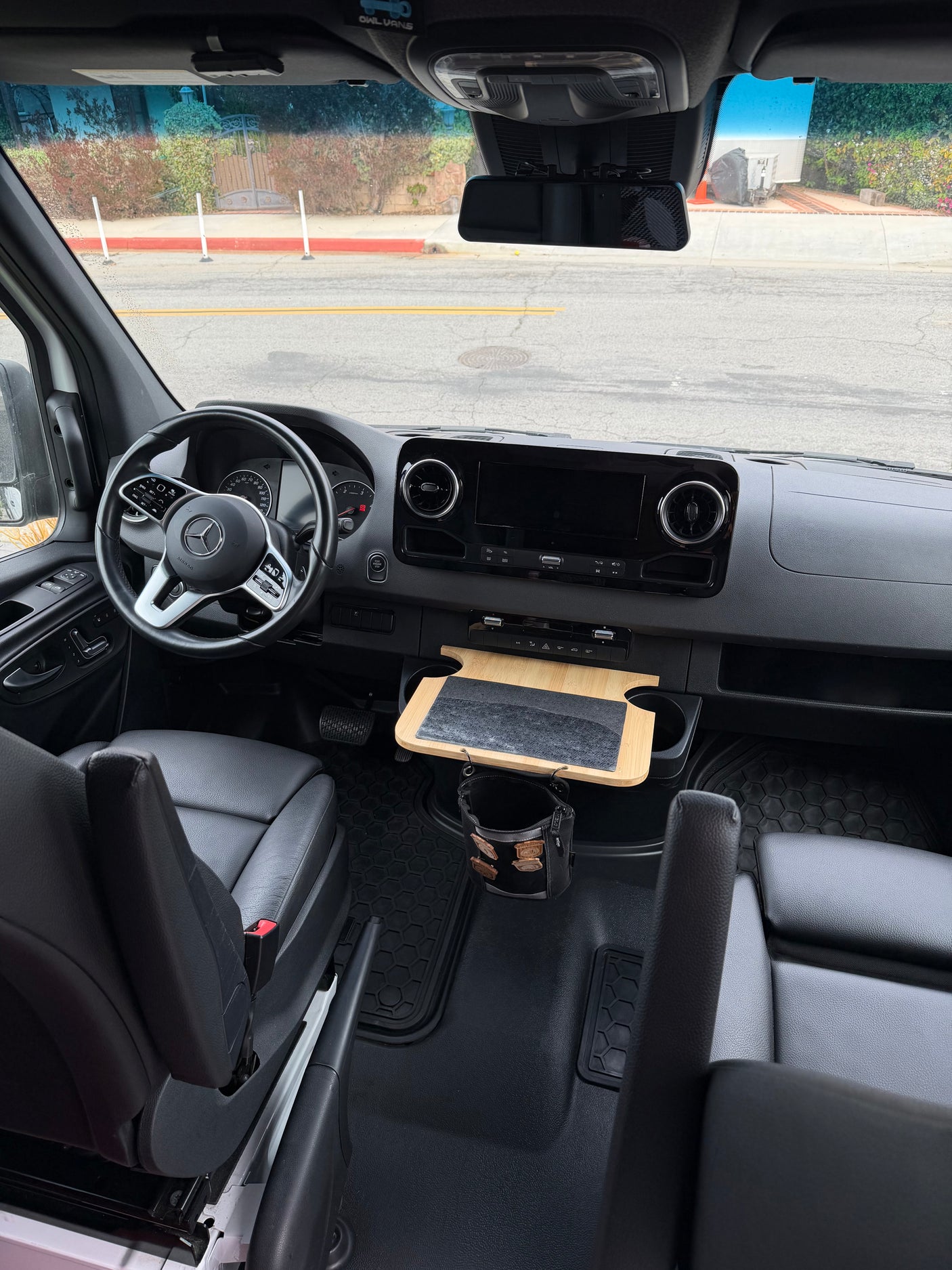 Inside an rv rental Mercedes Sprinter camper van: dashboard, steering wheel, black leather seats, and a useful custom bamboo tray.