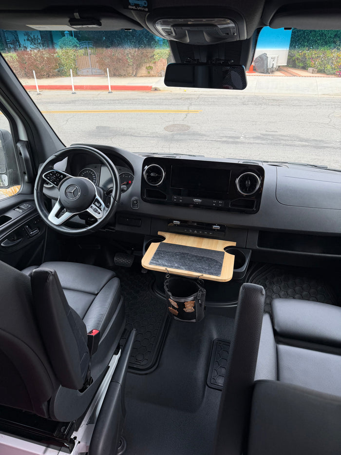 Inside an rv rental Mercedes Sprinter camper van: dashboard, steering wheel, black leather seats, and a useful custom bamboo tray.