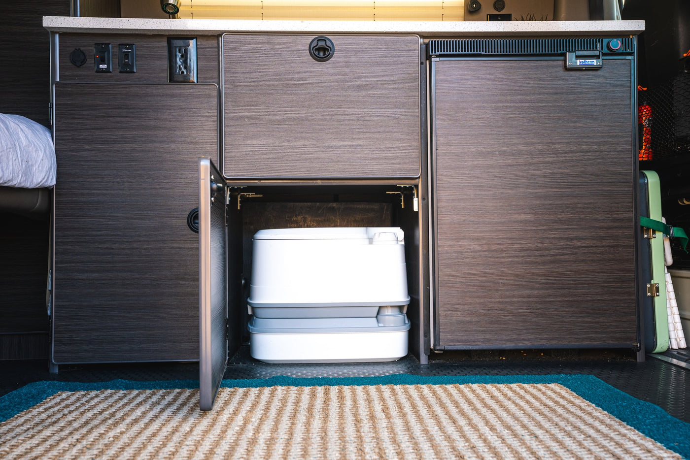 Inside this rv rental, a discreet cabinet reveals a portable toilet, flanked by a compact fridge and storage, perfect for campervan adventures. — photo 9