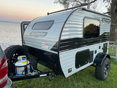 A light gray Sunray Sport travel trailer with off-road tires, perfect for an RV rental for lakeside camping at dusk.