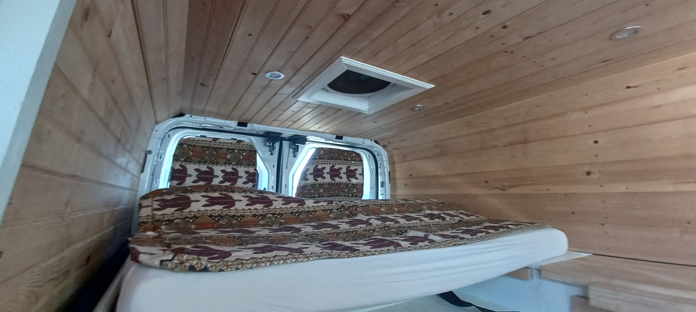 Cozy RV rental interior with wood paneling, a patterned bed, and seats in this converted camper van.