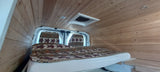 Cozy RV rental interior with wood paneling, a patterned bed, and seats in this converted camper van.