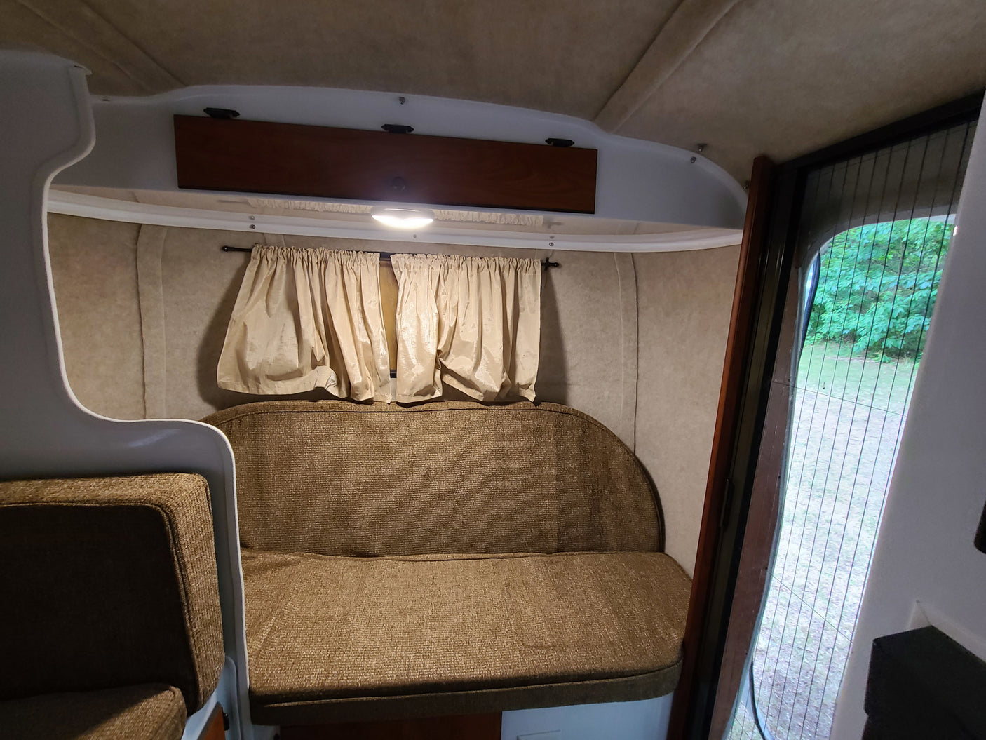 Inside an RV rental: upholstered bench, curtains, and an inviting view through the screen door, perfect for travel.